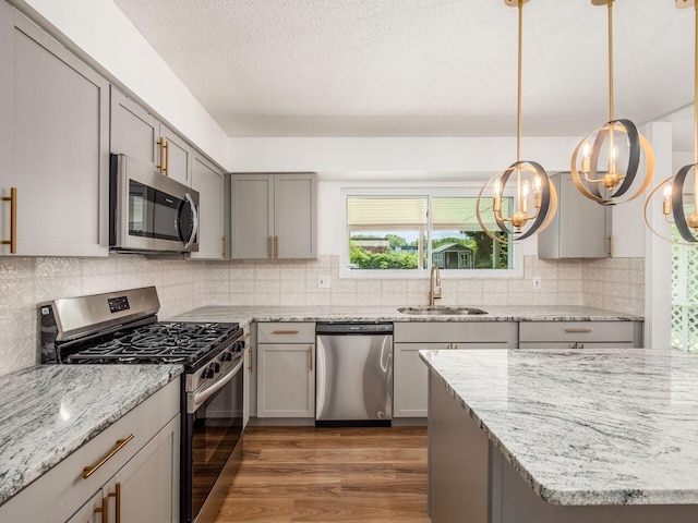 kitchen with sink, dark wood-type flooring, stainless steel appliances, an inviting chandelier, and decorative light fixtures