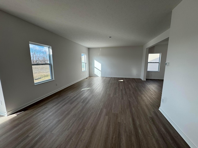 empty room featuring a textured ceiling, dark hardwood / wood-style flooring, and a wealth of natural light