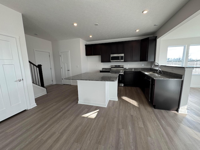 kitchen with a center island, sink, stainless steel appliances, and dark stone counters