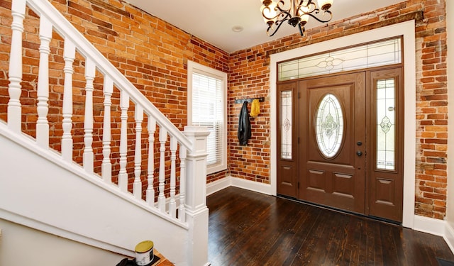 foyer featuring dark hardwood / wood-style flooring, a wealth of natural light, a notable chandelier, and brick wall