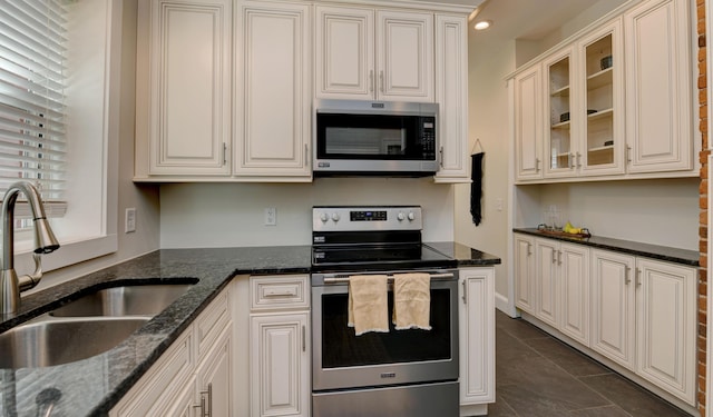 kitchen with dark tile patterned flooring, sink, stainless steel appliances, and dark stone counters