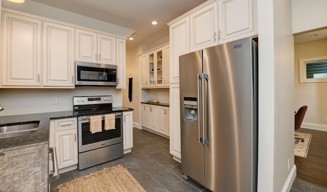 kitchen with appliances with stainless steel finishes, dark tile patterned flooring, dark stone counters, and sink