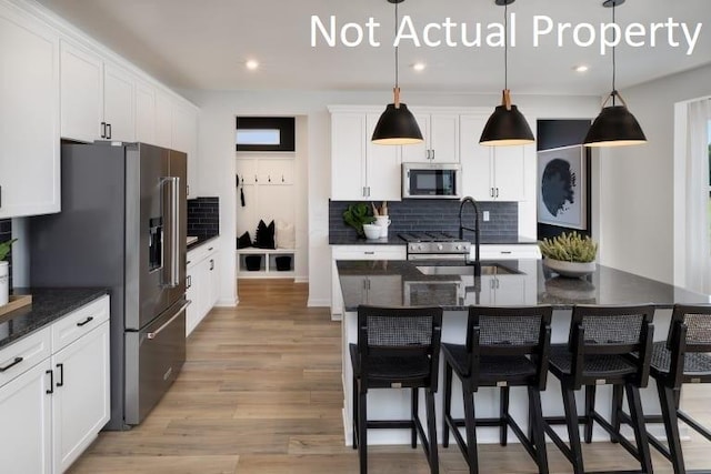 kitchen featuring a kitchen island with sink, sink, hanging light fixtures, decorative backsplash, and stainless steel appliances