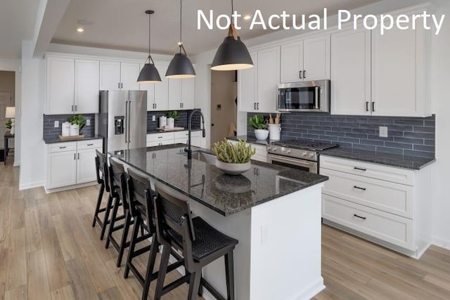 kitchen with a center island with sink, decorative backsplash, white cabinetry, and appliances with stainless steel finishes