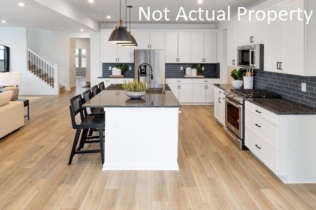 kitchen featuring white cabinets, stainless steel appliances, a kitchen island with sink, and hanging light fixtures