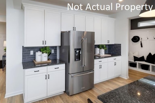 kitchen with light hardwood / wood-style flooring, dark stone countertops, tasteful backsplash, high quality fridge, and white cabinets