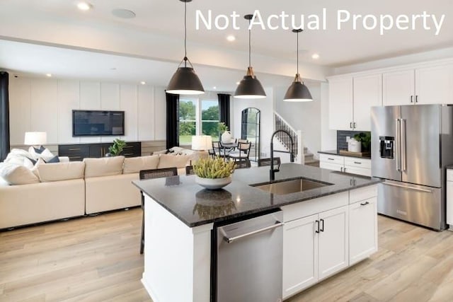 kitchen featuring appliances with stainless steel finishes, decorative light fixtures, sink, white cabinets, and a center island with sink