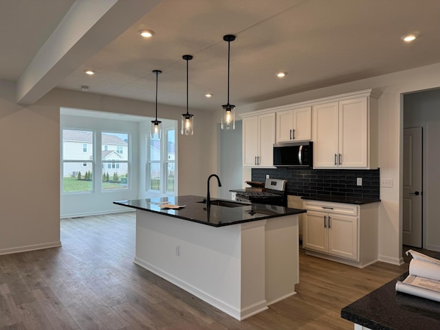 kitchen with white cabinetry, a kitchen island with sink, sink, and hanging light fixtures