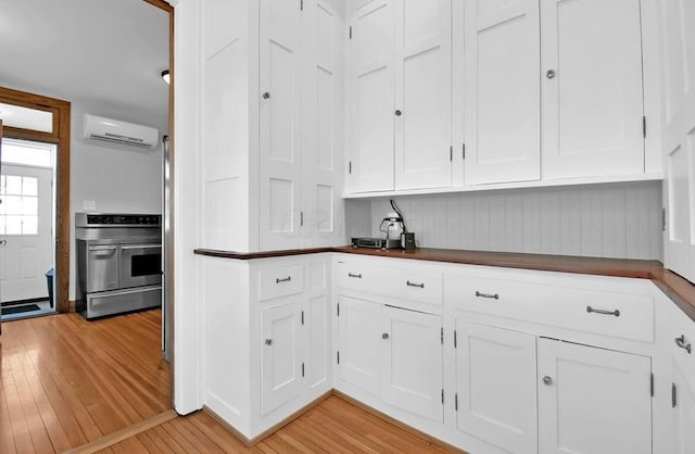 kitchen featuring a wall mounted air conditioner, oven, white cabinetry, and light wood-type flooring