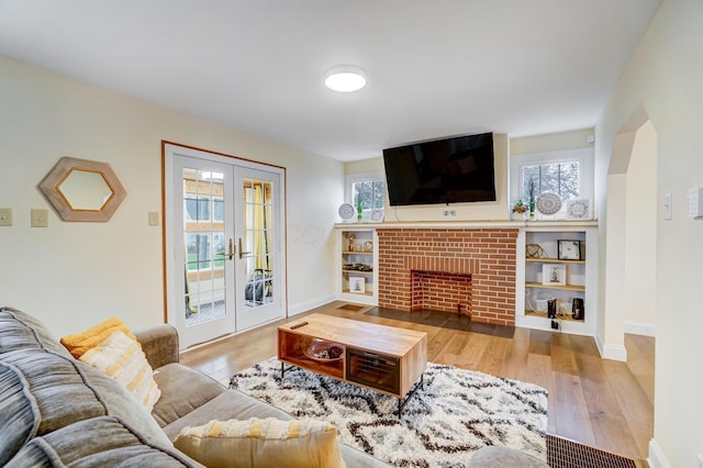 living room featuring a brick fireplace, plenty of natural light, light wood-type flooring, and french doors