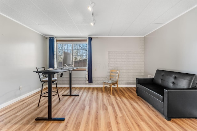 interior space featuring rail lighting, ornamental molding, brick wall, and light hardwood / wood-style flooring