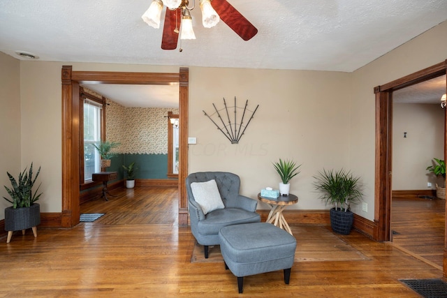 living area featuring ceiling fan, wood-type flooring, and a textured ceiling