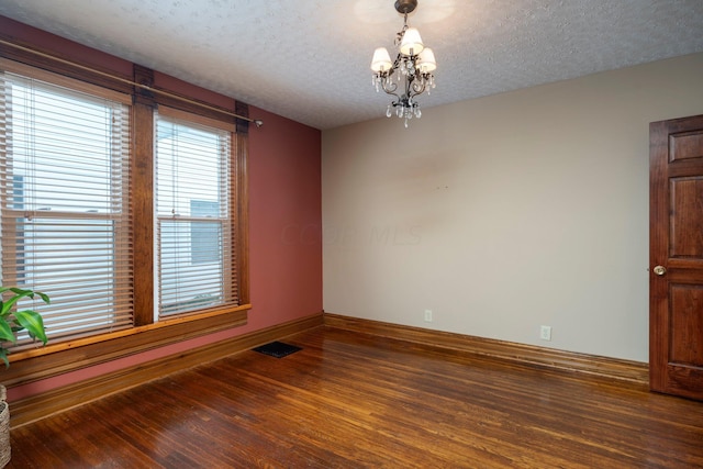 unfurnished room with dark hardwood / wood-style flooring, a textured ceiling, and an inviting chandelier