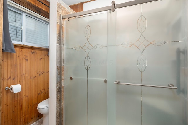 bathroom with toilet, a shower with door, and wooden walls