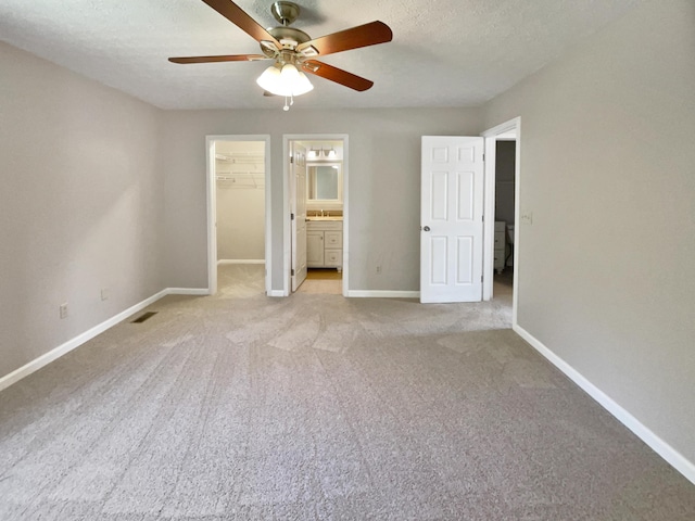 unfurnished bedroom with ceiling fan, light colored carpet, a walk in closet, and ensuite bathroom