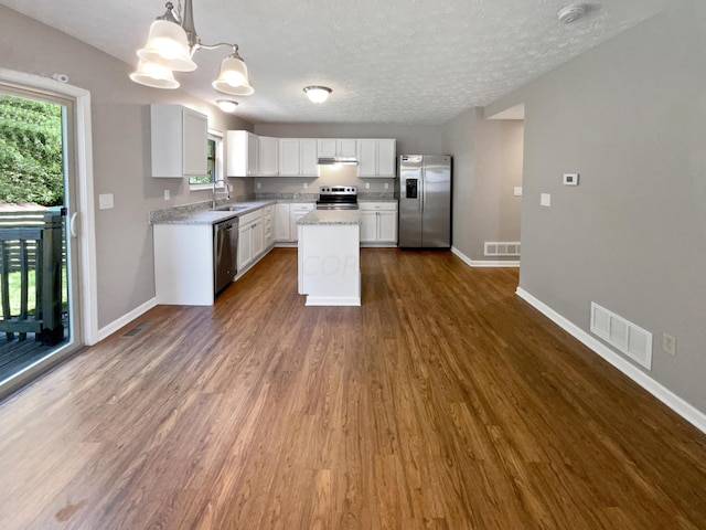 kitchen featuring pendant lighting, dark wood-type flooring, white cabinets, a kitchen island, and stainless steel appliances