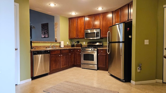 kitchen featuring stone counters, sink, a textured ceiling, and appliances with stainless steel finishes