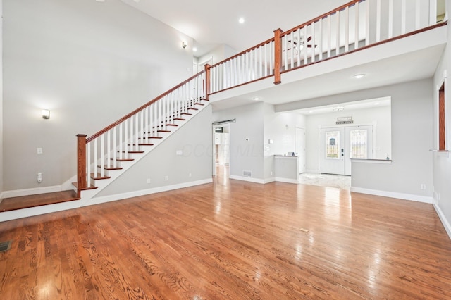 unfurnished living room with hardwood / wood-style flooring, a towering ceiling, and french doors