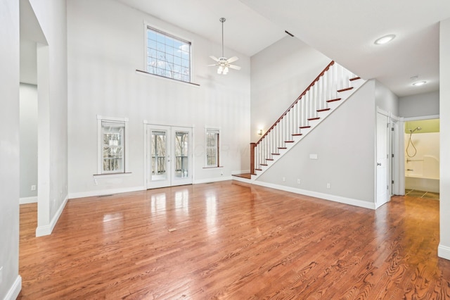 unfurnished living room with ceiling fan, french doors, wood-type flooring, and a high ceiling