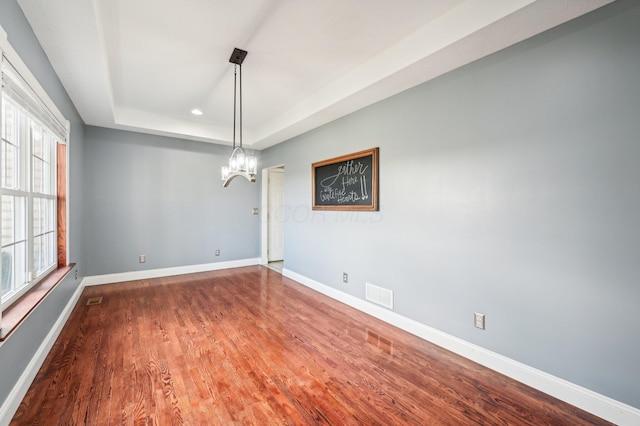 empty room with a raised ceiling, a notable chandelier, and hardwood / wood-style flooring