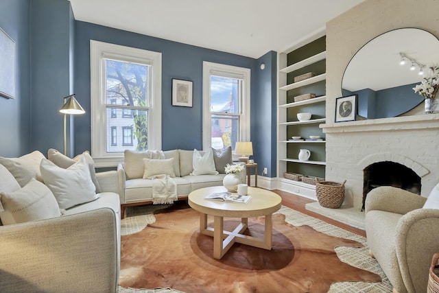 living room with built in features, wood-type flooring, and a brick fireplace