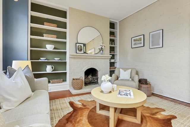 living room with built in shelves, wood-type flooring, and a brick fireplace