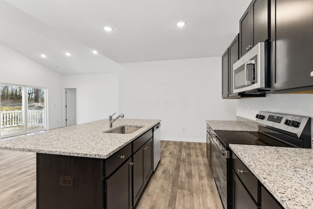 kitchen with light wood-type flooring, stainless steel appliances, vaulted ceiling, a kitchen island with sink, and sink