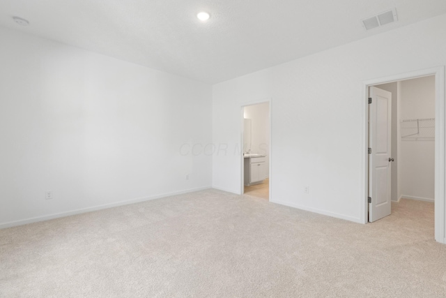 unfurnished bedroom featuring light carpet, connected bathroom, a spacious closet, and a closet