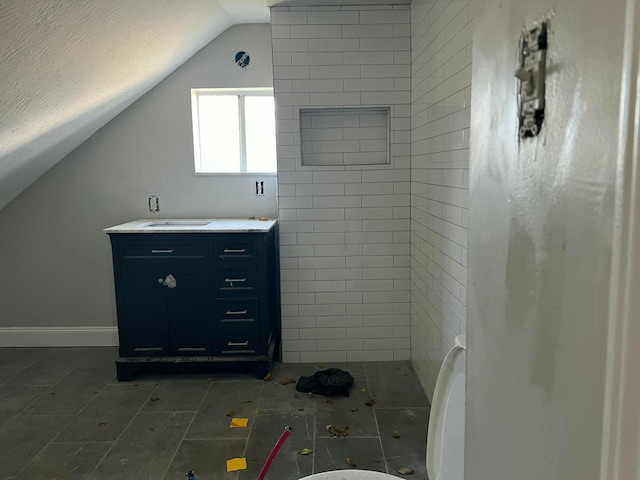 bathroom featuring vanity, a tile shower, and vaulted ceiling