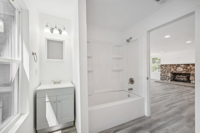 bathroom featuring hardwood / wood-style floors, vanity, a stone fireplace, and shower / bathtub combination