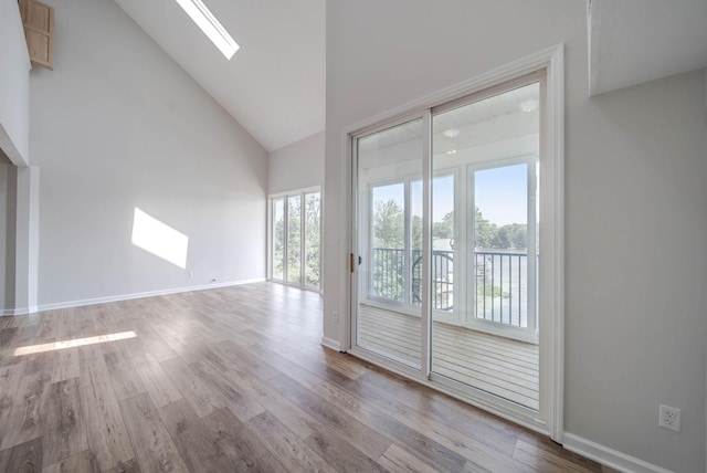 interior space featuring a skylight, light hardwood / wood-style flooring, high vaulted ceiling, and a healthy amount of sunlight