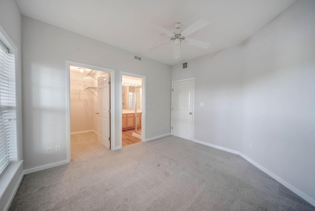 unfurnished bedroom with light carpet, a walk in closet, a closet, and ceiling fan