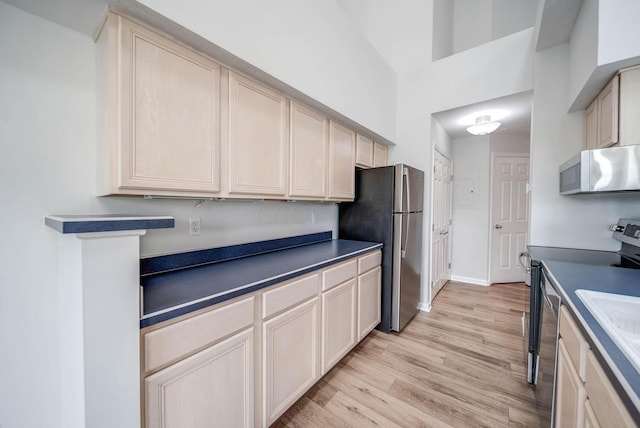 kitchen featuring light brown cabinets, light wood-type flooring, stainless steel appliances, and a high ceiling