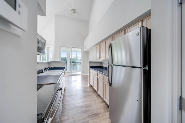 kitchen featuring high vaulted ceiling, sink, light wood-type flooring, light brown cabinetry, and appliances with stainless steel finishes