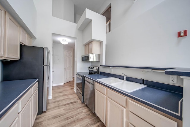 kitchen featuring sink, a towering ceiling, stainless steel appliances, and light hardwood / wood-style flooring