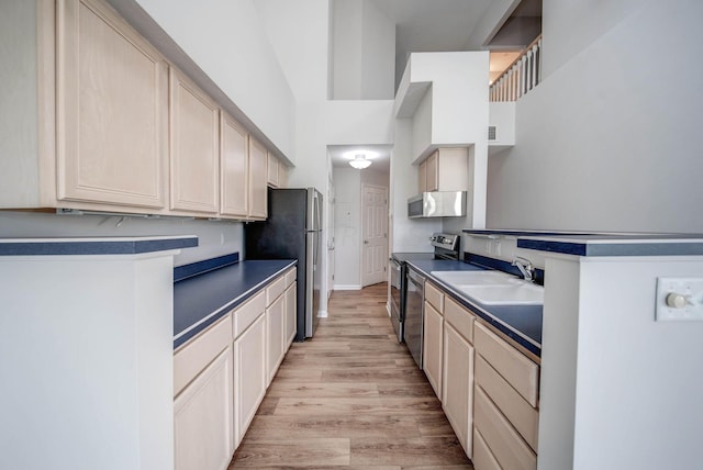 kitchen featuring light brown cabinets, sink, light hardwood / wood-style flooring, a towering ceiling, and stainless steel appliances