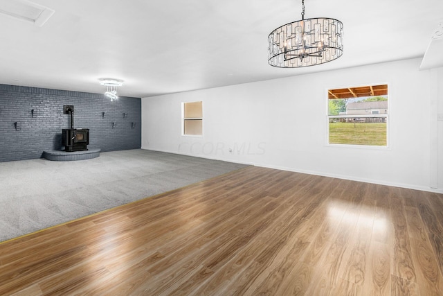 unfurnished living room featuring a wood stove, an inviting chandelier, brick wall, and hardwood / wood-style flooring