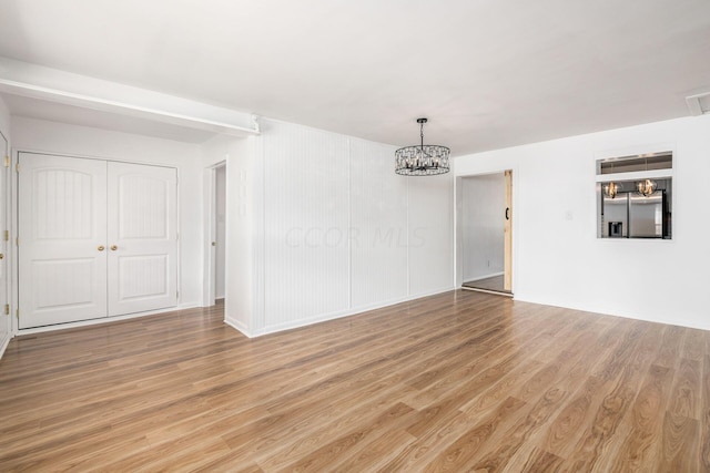 empty room with light hardwood / wood-style floors and an inviting chandelier