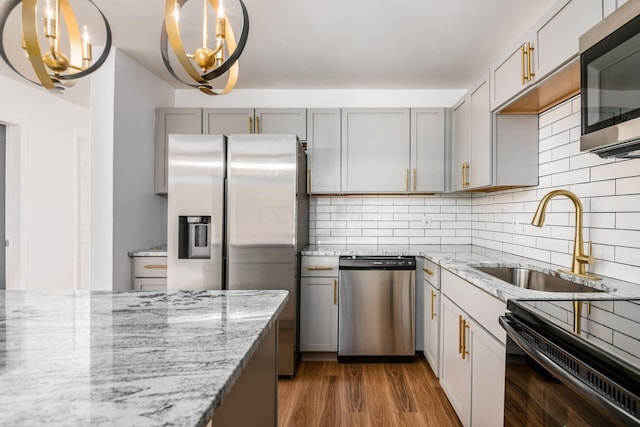 kitchen with dark wood-type flooring, sink, hanging light fixtures, light stone counters, and stainless steel appliances