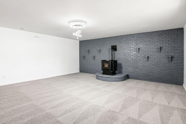 unfurnished living room with a wood stove, light colored carpet, and brick wall