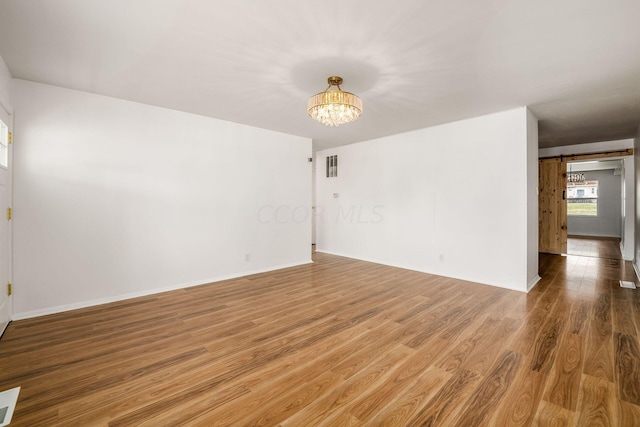 unfurnished room featuring a notable chandelier and hardwood / wood-style flooring