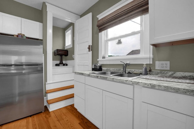 kitchen with white cabinetry, light wood-type flooring, sink, and stainless steel refrigerator