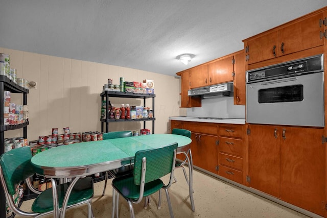 kitchen featuring wood walls, oven, stovetop, and a textured ceiling