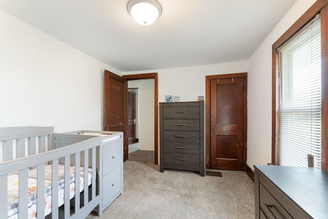 bedroom featuring light colored carpet and a nursery area