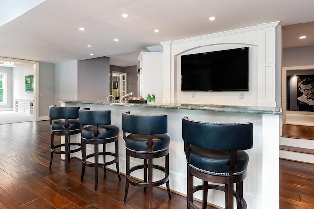 kitchen featuring white cabinetry, light stone counters, dark hardwood / wood-style floors, kitchen peninsula, and a breakfast bar