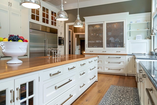 kitchen with wooden counters, pendant lighting, light hardwood / wood-style flooring, white cabinets, and built in refrigerator