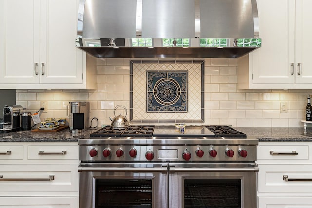 kitchen with island exhaust hood, dark stone countertops, white cabinets, and range with two ovens