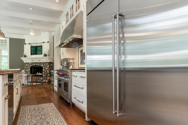 kitchen featuring high quality appliances, a fireplace, beamed ceiling, dark hardwood / wood-style flooring, and white cabinetry