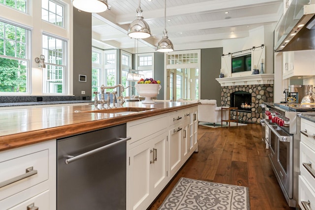 kitchen with white cabinetry, stainless steel appliances, a stone fireplace, dark hardwood / wood-style flooring, and pendant lighting