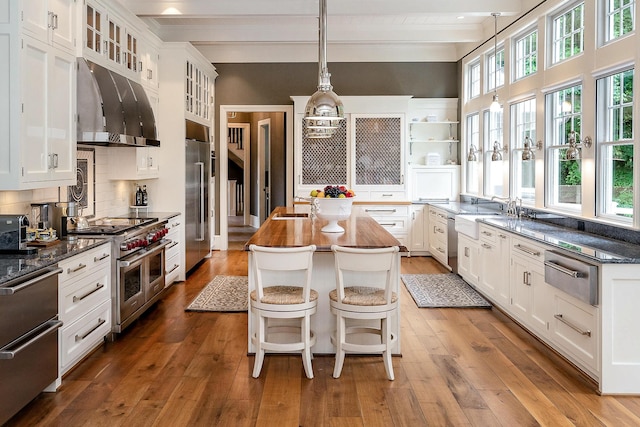 kitchen with ventilation hood, dark hardwood / wood-style floors, beam ceiling, premium appliances, and a kitchen island